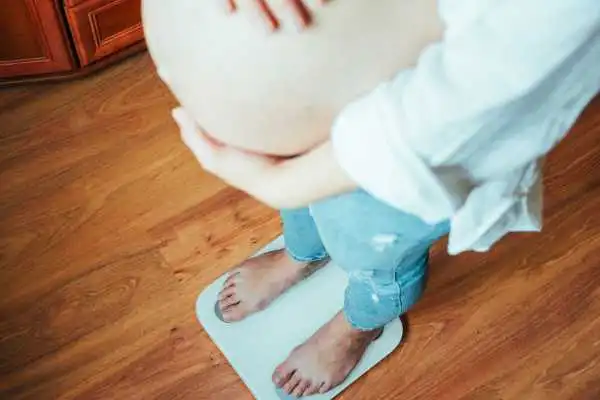 Image of woman weighing herself and experiencing weight gain through pregnancy Kirkcaldy
